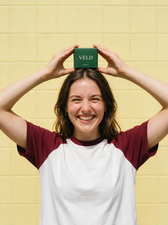 Vrouw houdt een doosje boven haar hoofd tegen geel